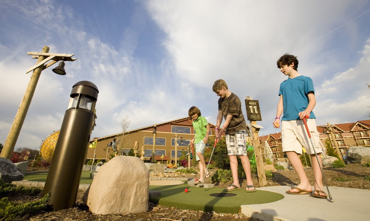 Three older boys playing mini golf outside