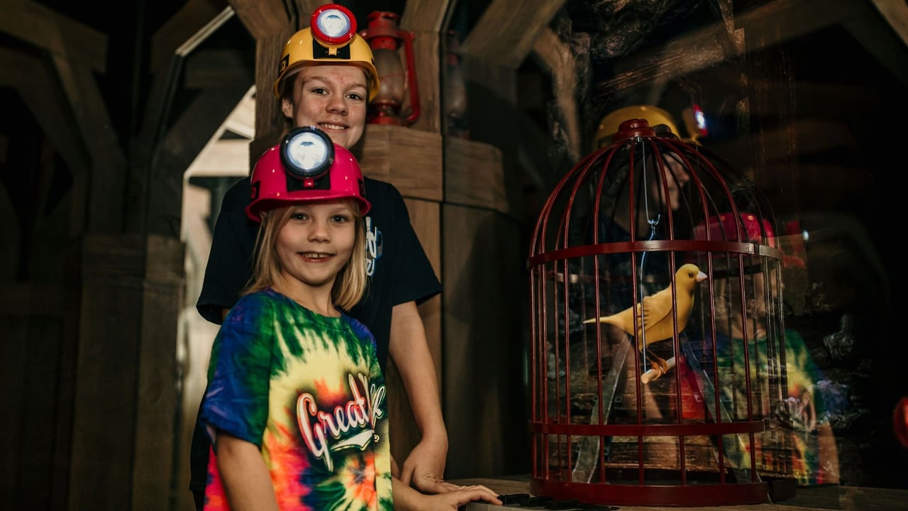 Two kids in mining helmets smiling near a birdcage display