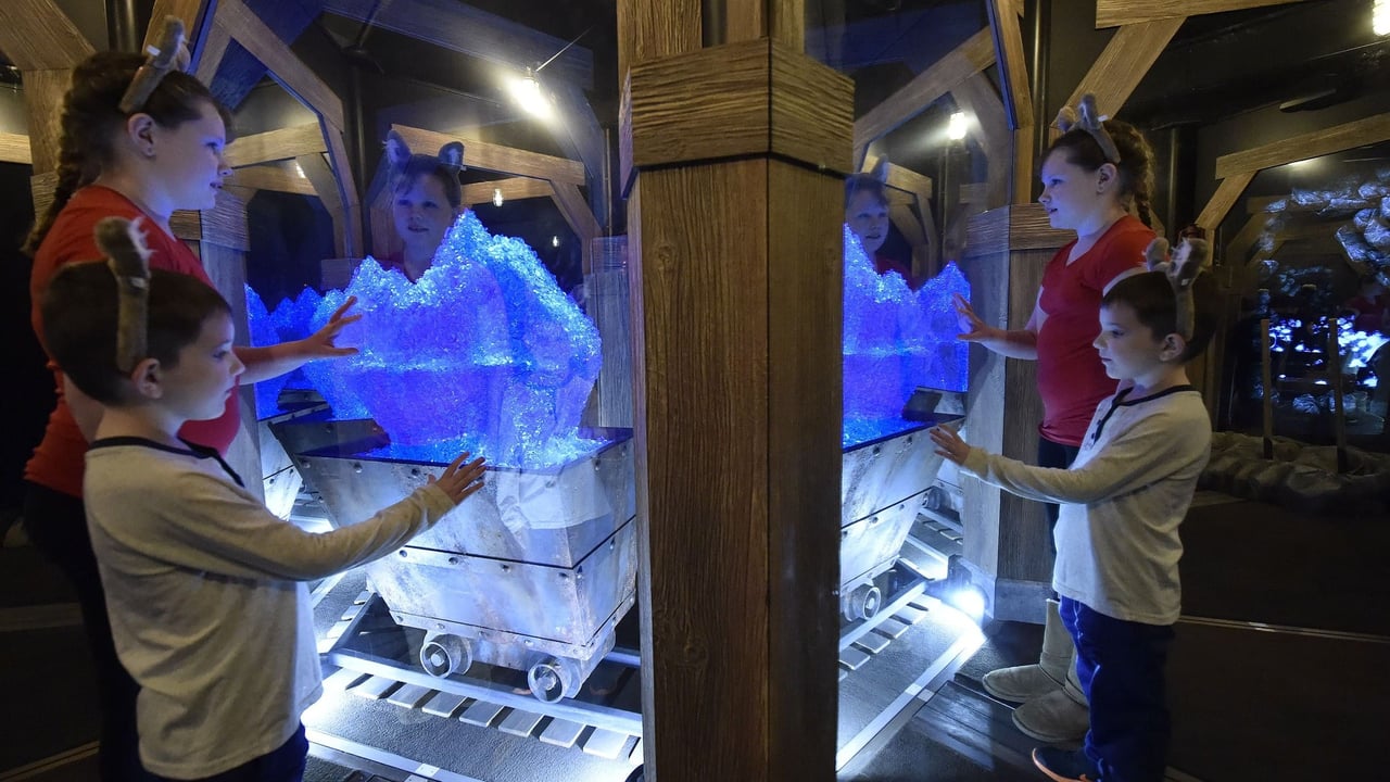 Family interacting with glowing blue crystal in a mine exhibit