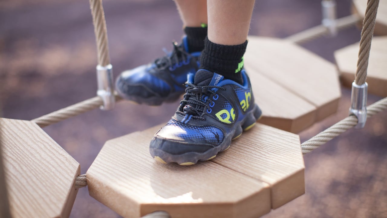 Close-up of kid’s sneakers stepping on wooden rope bridge planks