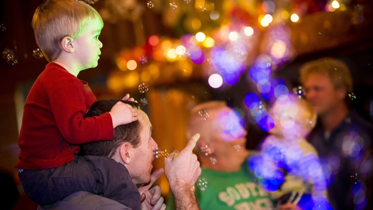 Boy is sitting on his father's shoulders and enjoying the dance party