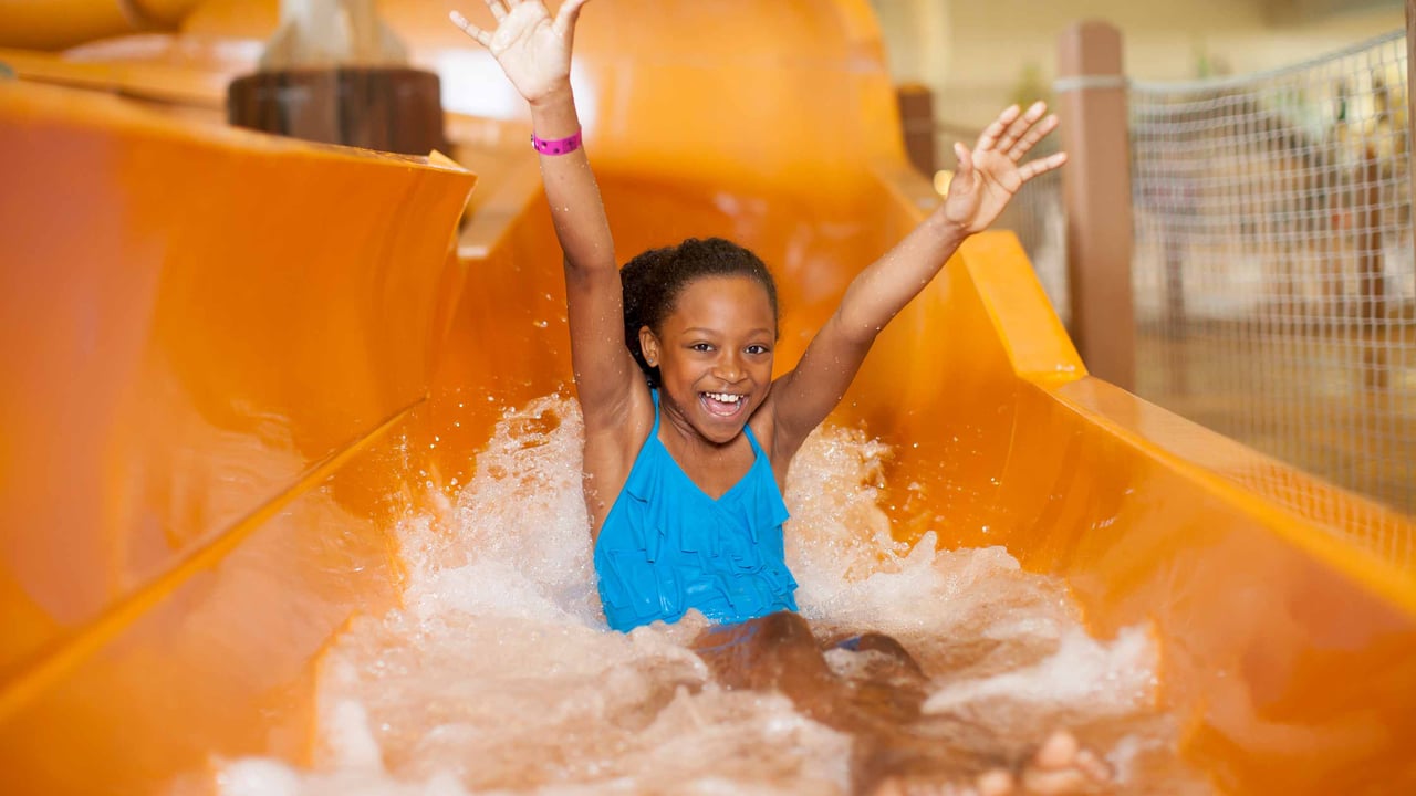 A young girl with her arms up going down an orange water slide