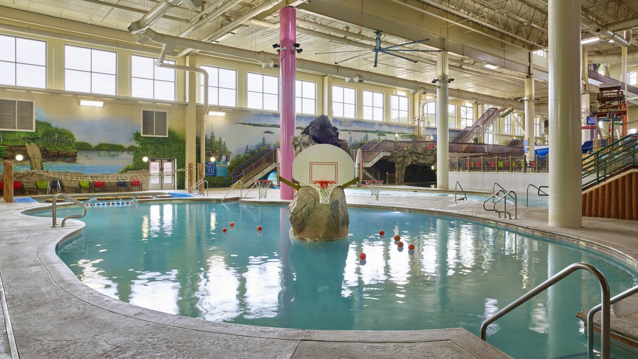 A spacious indoor pool featuring a basketball hoop and a fun water slide for fun activities.