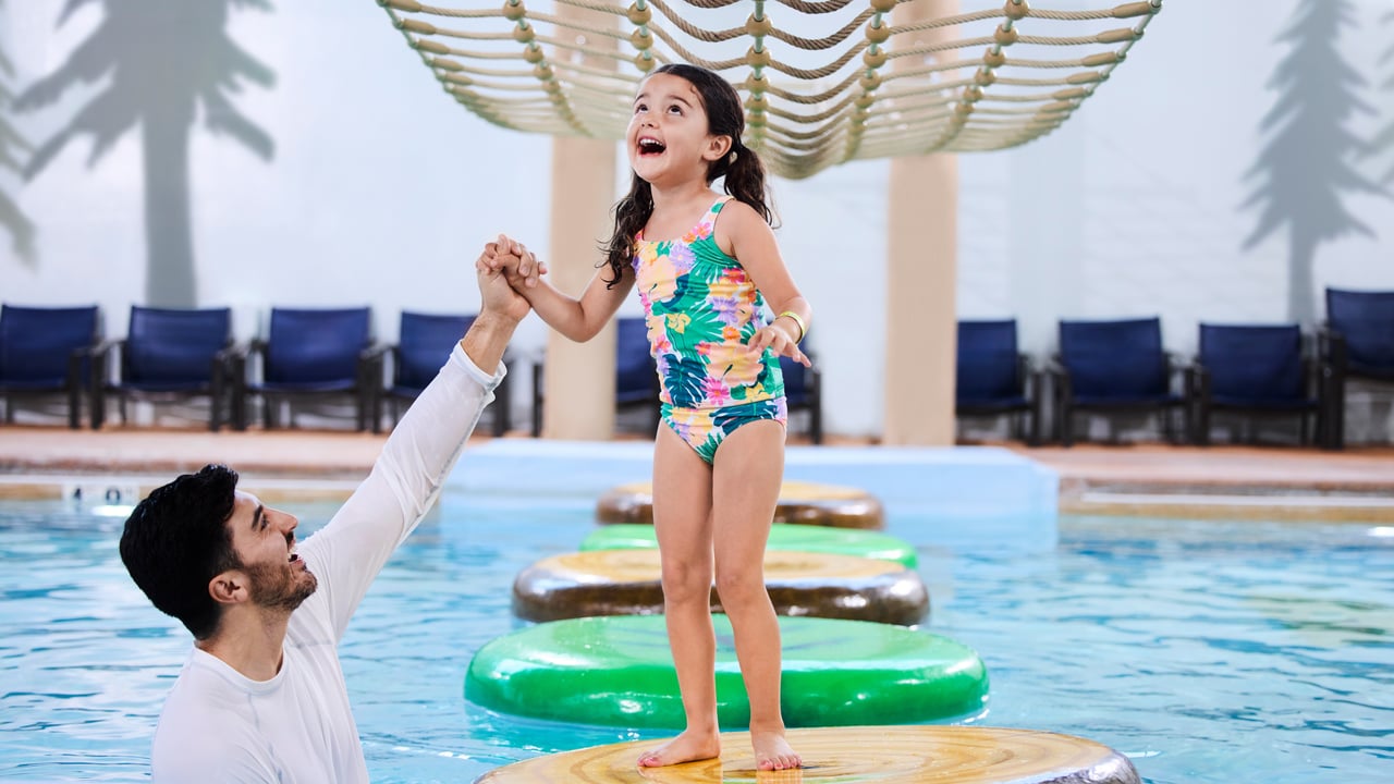 A girl balances on a lily pad float in indoor pool