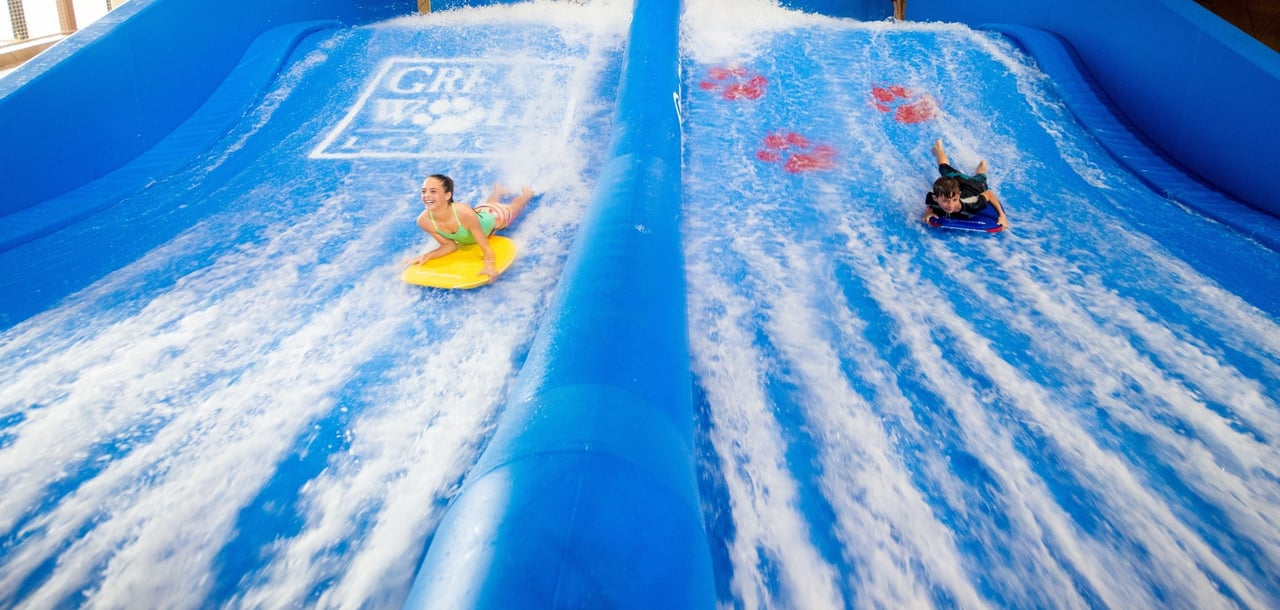 On the left, a girl on a yellow boogie board and on the right a boy on a blue boogie board racing down the waterslide