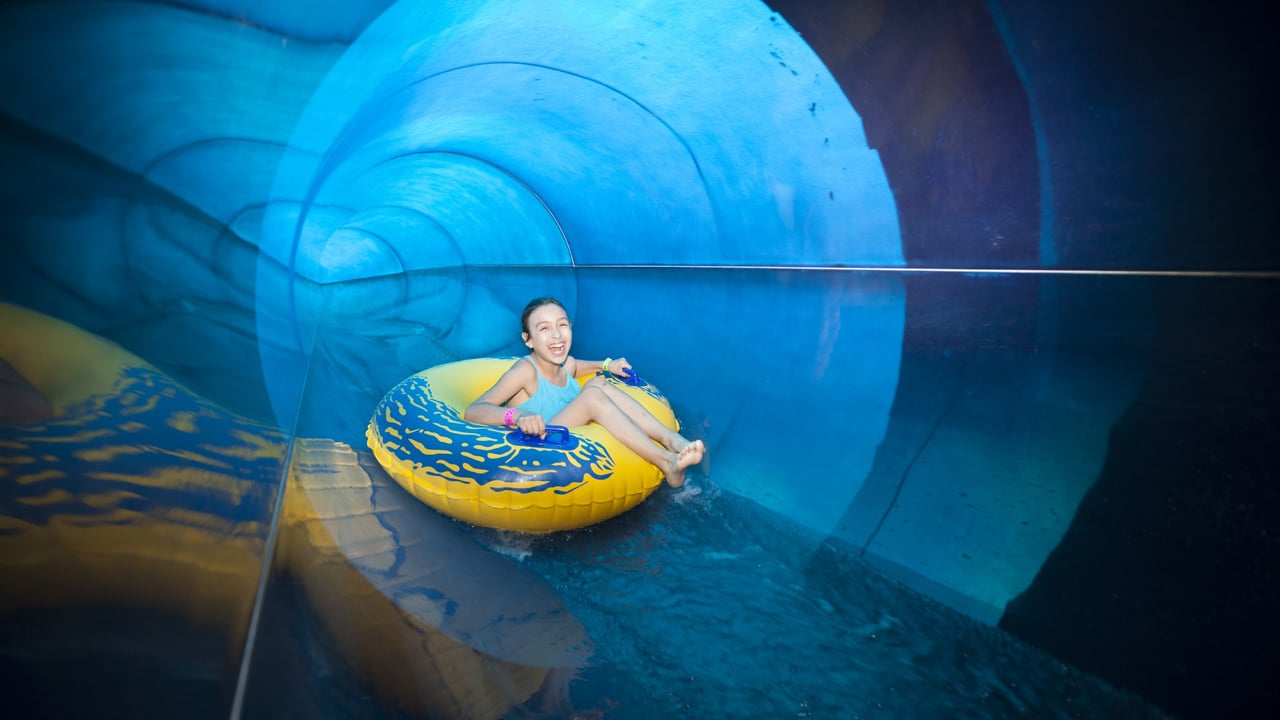 teen on a yellow tube going down a blue water slide