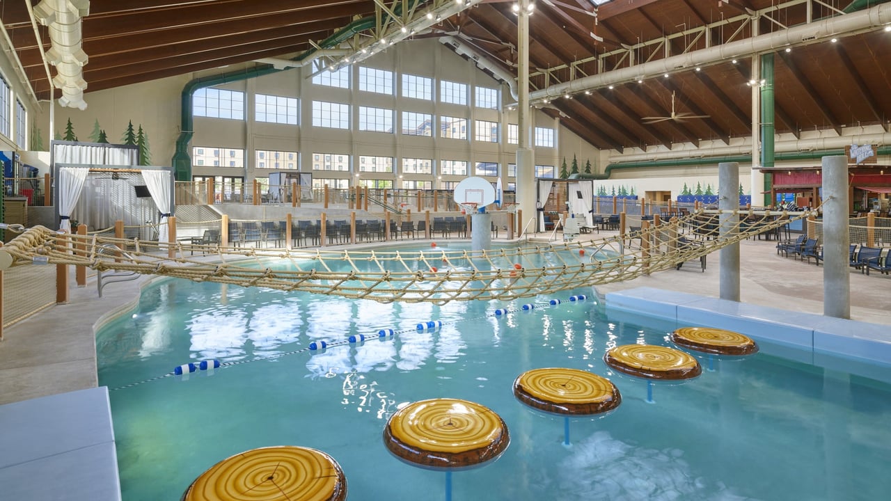 Indoor water park featuring a rope bridge and a large water slide surrounded by pools and playful water features