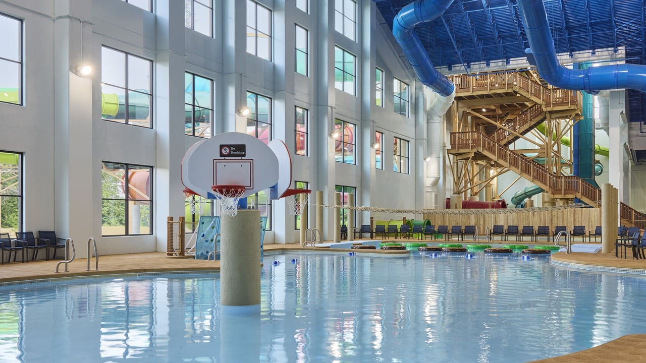 Families playing basketball in large indoor pool equipped with a colorful water slide