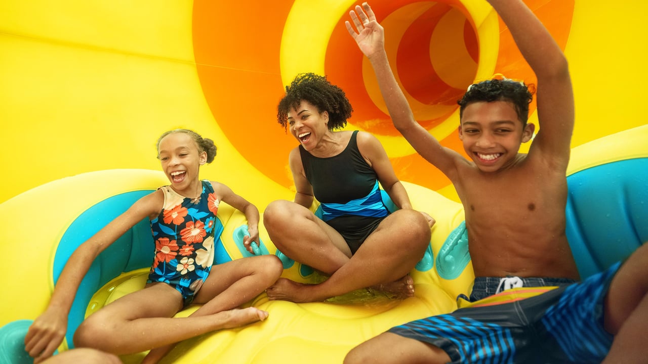 A woman and two children on a large raft going down an indoor water slide.