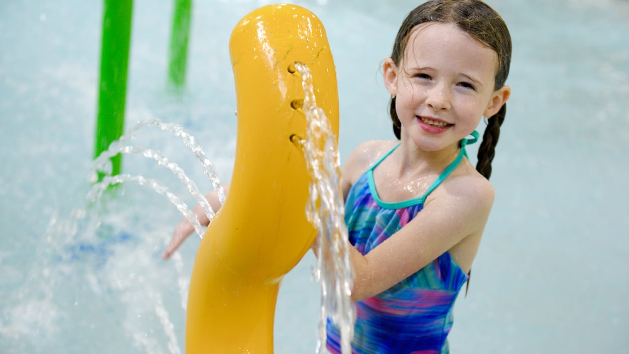 young girl in a knee-deep pool playing with a water spout