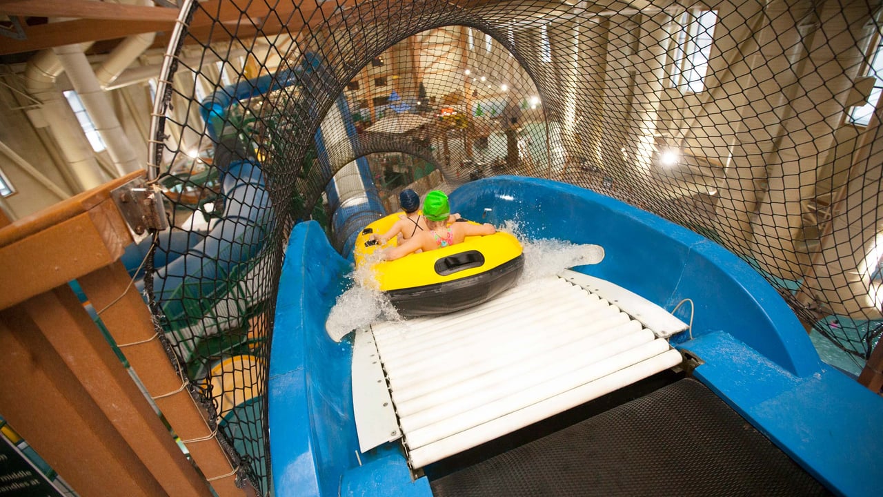 Two people in a yellow tandem raft beginning the decent on blue indoor water slide.