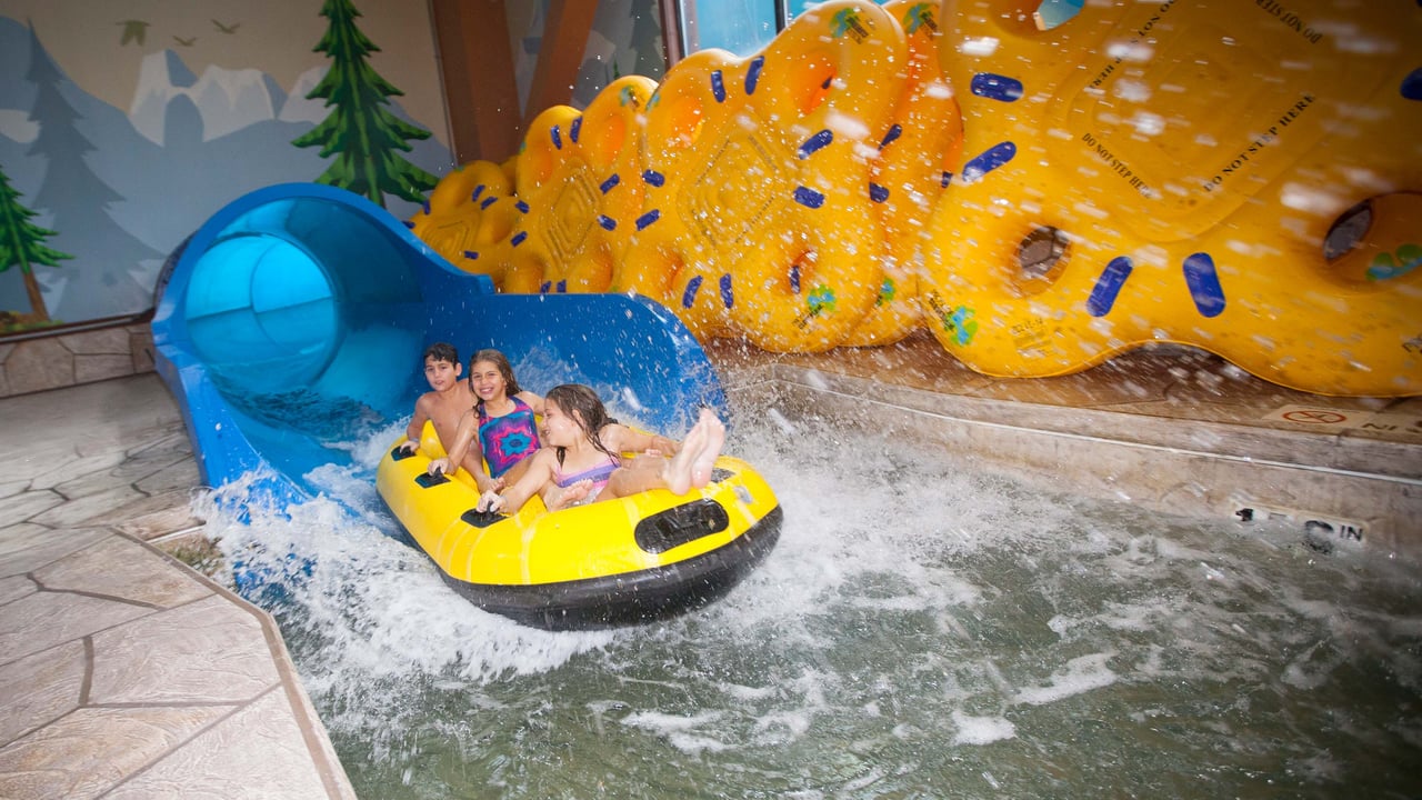 Three children in a yellow raft landing in a pool of water at the end of a indoor water slide.