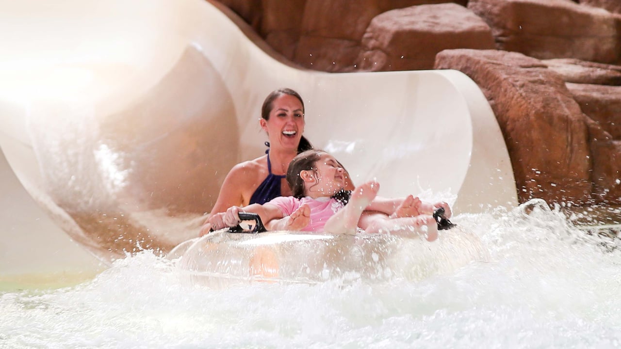 Woman and child riding down a white waterslide together surrounded by rocky decor