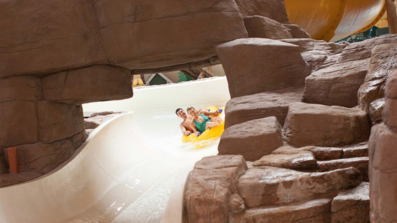 A couple in a tube race down the water slide surrounded by rock decor