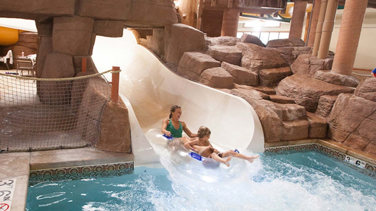 Woman and child in clear tubes riding down a white waterslide together surrounded by rocky decor