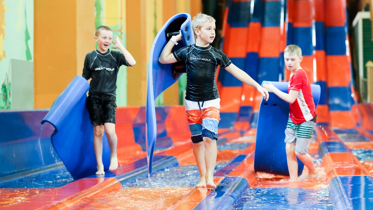 Three boys caring blue mats at the end of the water slide