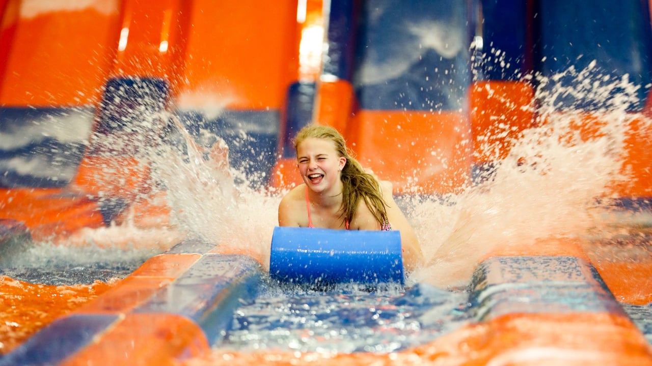 A young girl splashing down a waterslide laying on a blue mat
