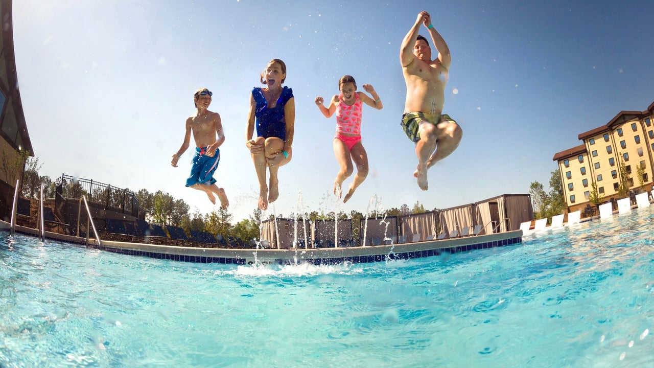 family jumping in the pool during summer time