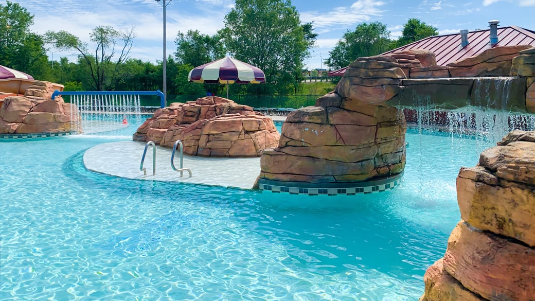 Outdoor pool with rock decor, a waterfall, umbrella, and a platform in the center for lounging