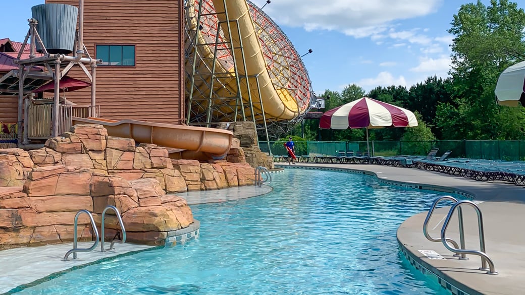 Outdoor pool with rock decor, a waterfall, umbrella, and a platform in the center for lounging