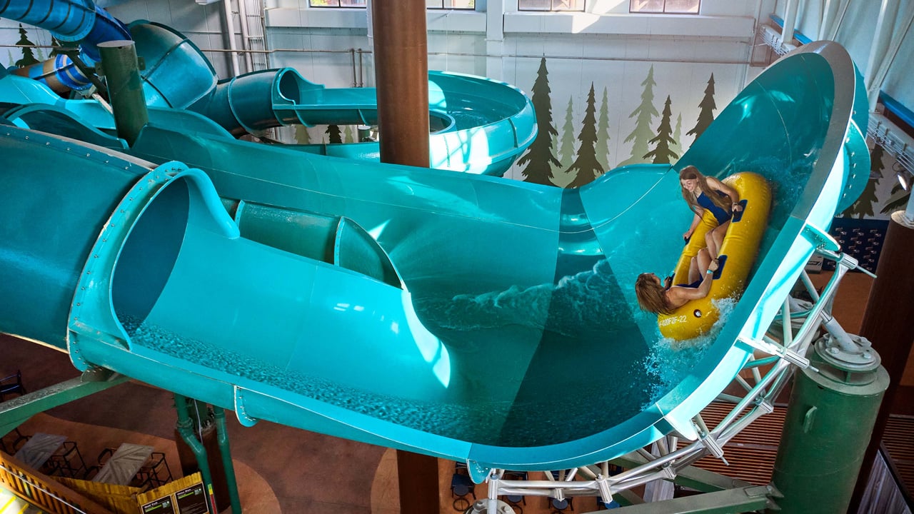 A woman and a child going on a raft ride down an indoor blue water slide.