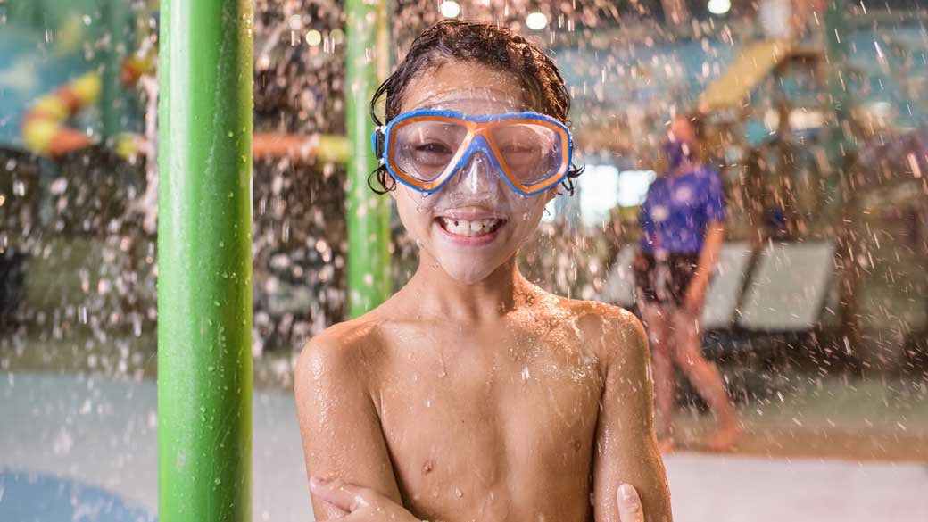 boy wearing swimming glasses and smiling standing under water droplets