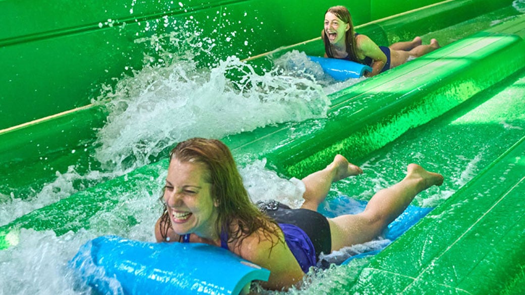 Two girls sliding down a green water slide at water park at the Great Wolf Lodge