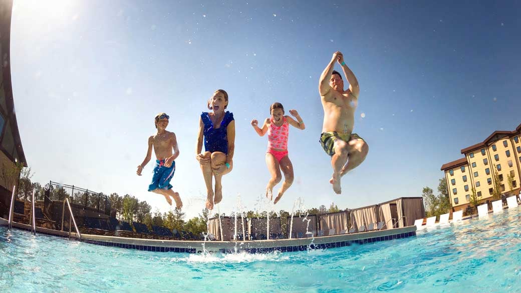 Happy family jumping into a pool together on a hot sunny day