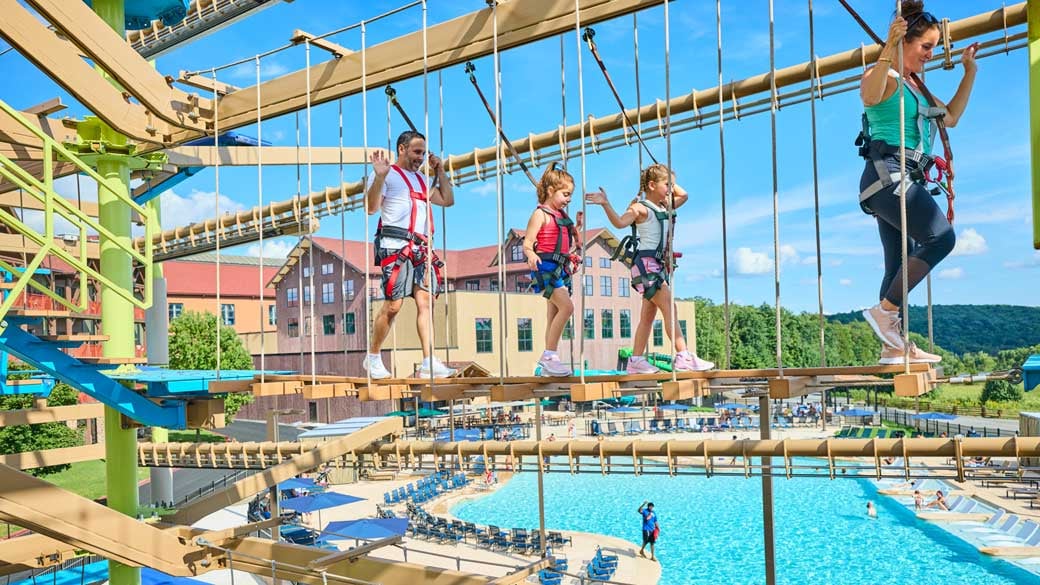Family going over an outdoor rope course with pool in the background