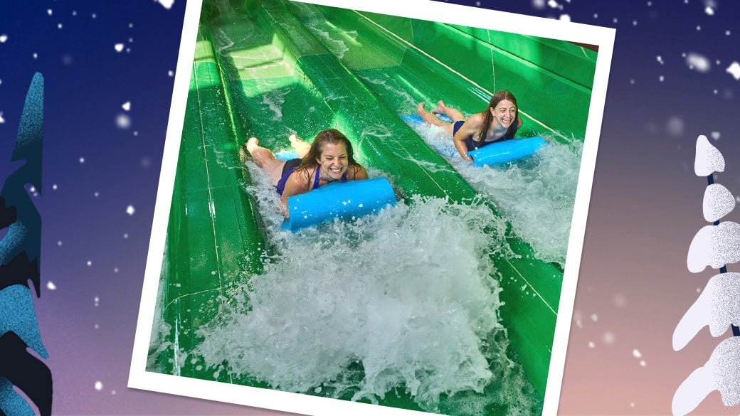 Two teens sliding down on a green slide into an indoor pool