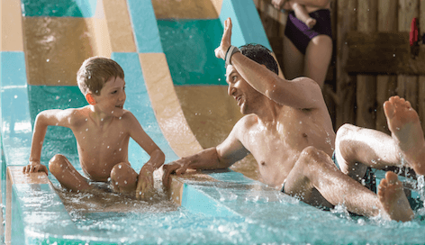 A father and son smile together while going down a slide 