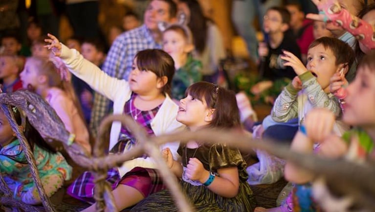 Kids raise their arms as they enjoy The Northwoods Friends Show in the lobby of a Great Wolf Lodge indoor water park and resorts.