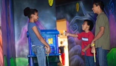 A family plays glow in the dark mini golf at Howl at the Moon Glow Golf at Great Wolf Lodge indoor water park and resort.