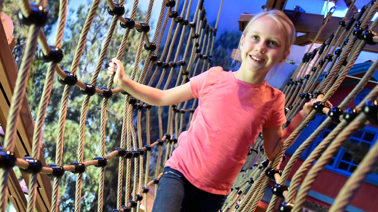 Young girl with a pink shirt navigating indoor ropes course