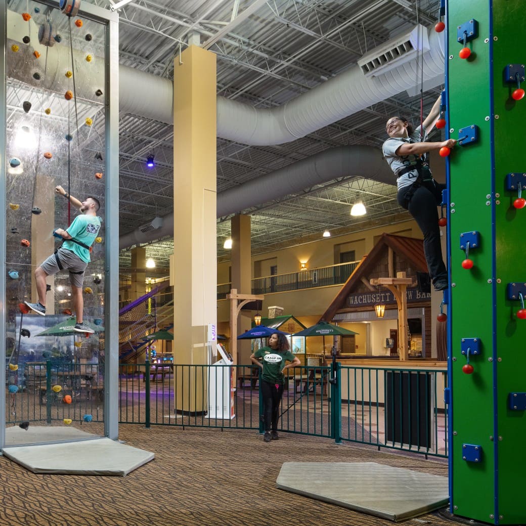 Family climbing an indoor rock wall with safety harnesses