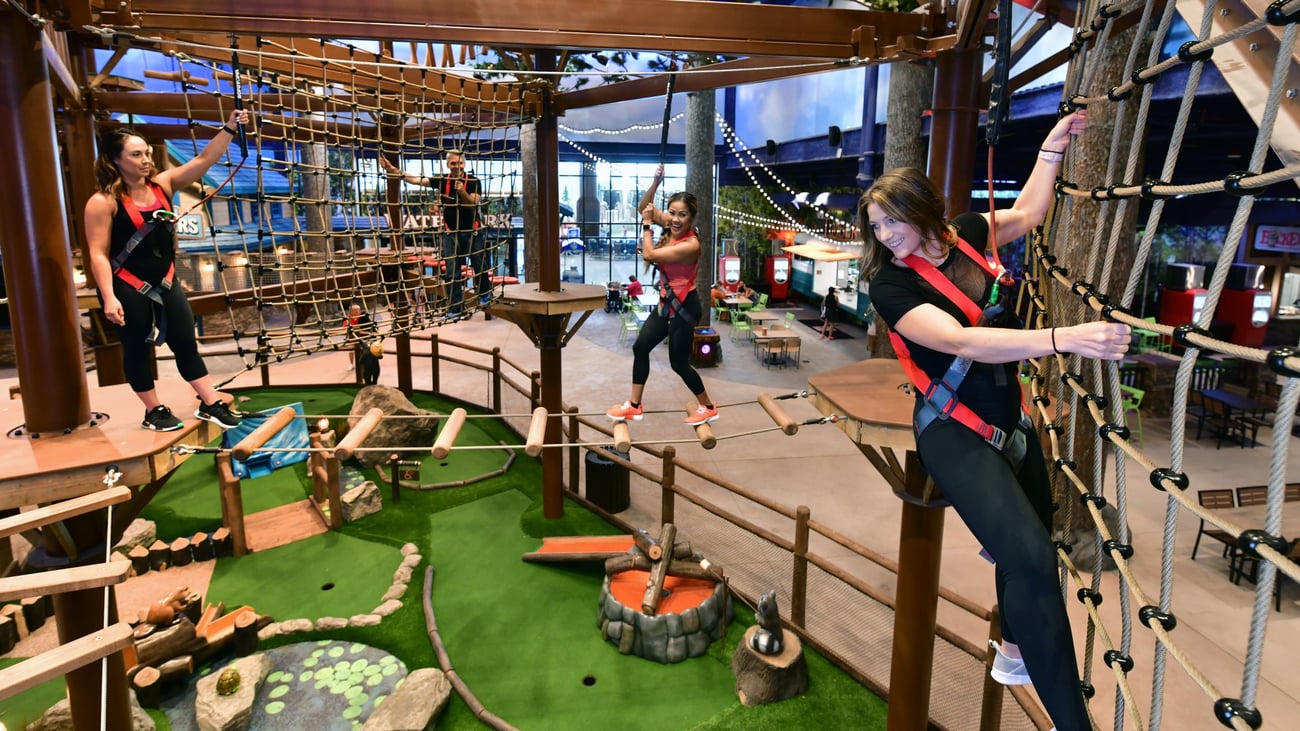 Three women navigating indoor ropes course with harnesses