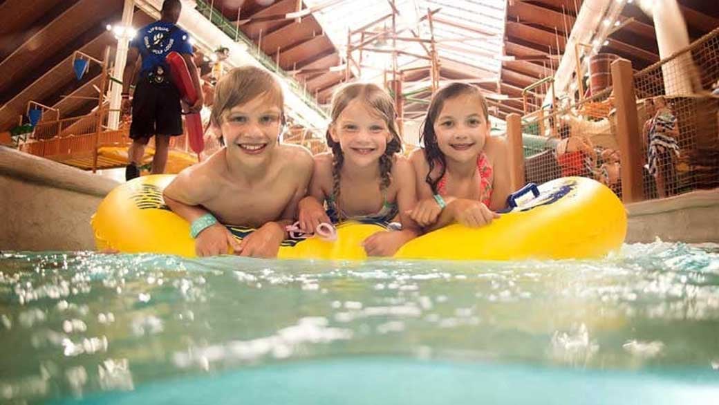 three smiling kids on a yellow tube enjoying the lazy river