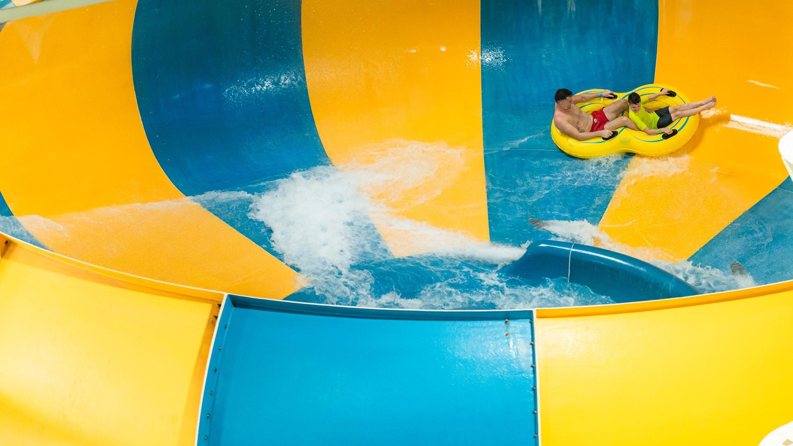 A father and son going down the Coyote Cannon water slide together on a yellow raft.