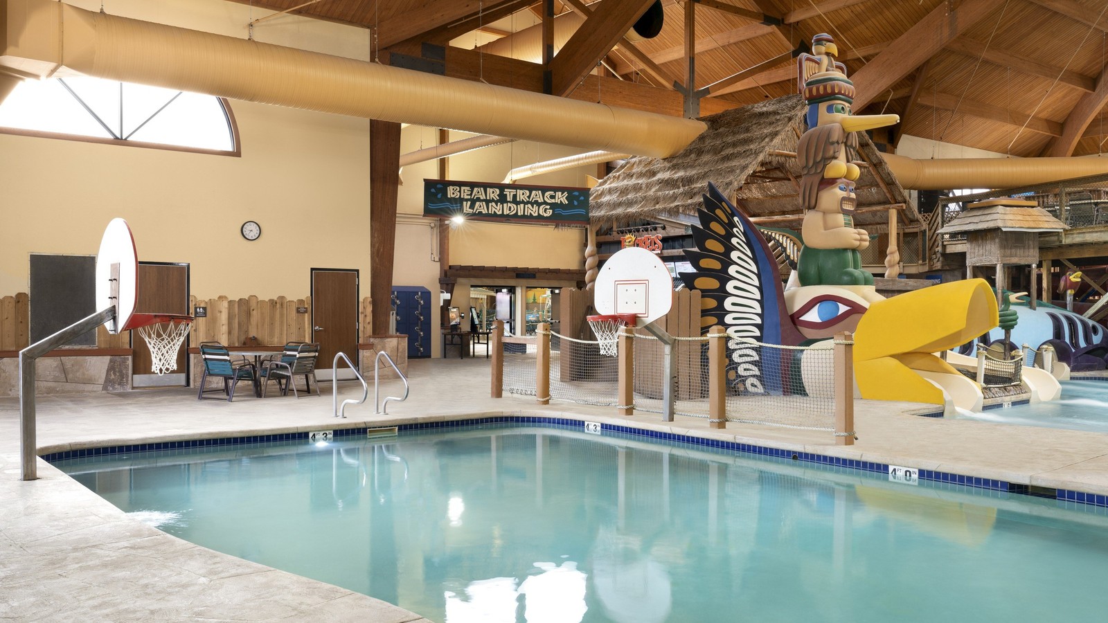Indoor pool featuring a water slide and a basketball hoop for recreational activities.