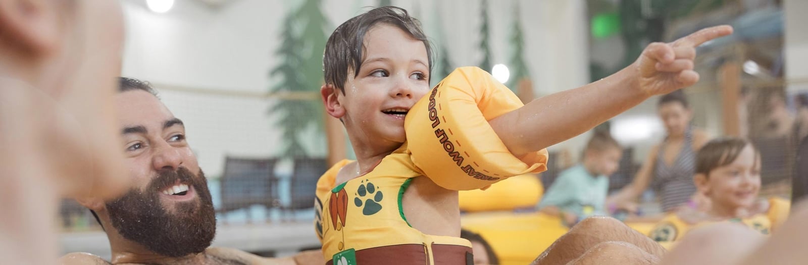 A boy smiles and points while his dad reacts with amazement in the water park at Great Wolf..