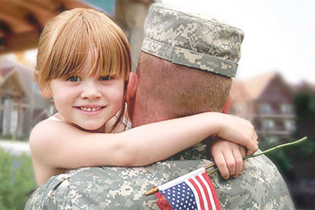 A father in military clothing holds his daughter who is smiling