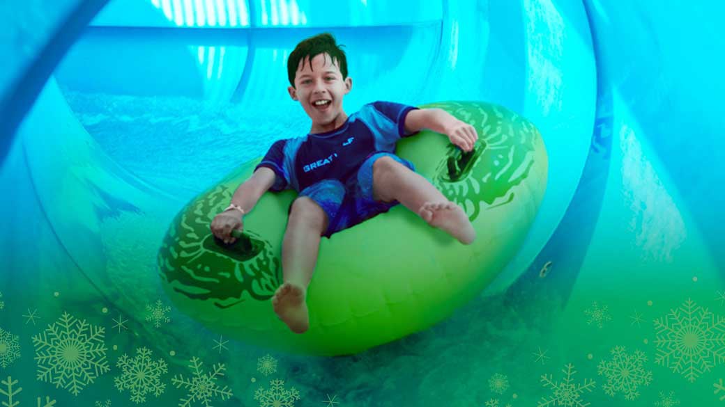 a young boy sliding down into a pool in a green tube