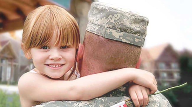 A father in military clothing holds his daughter who is smiling