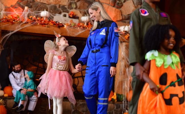 Child in fairy costume meeting astronaut character indoors.