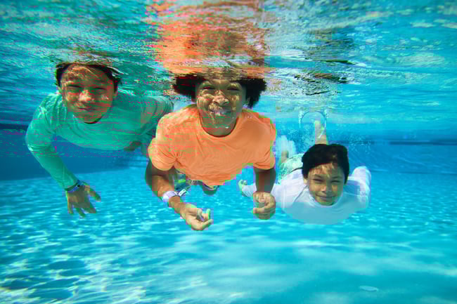 Three children smiling underwater in a swimming pool