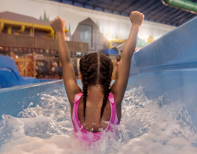 Child celebrating in water slide at indoor water park.