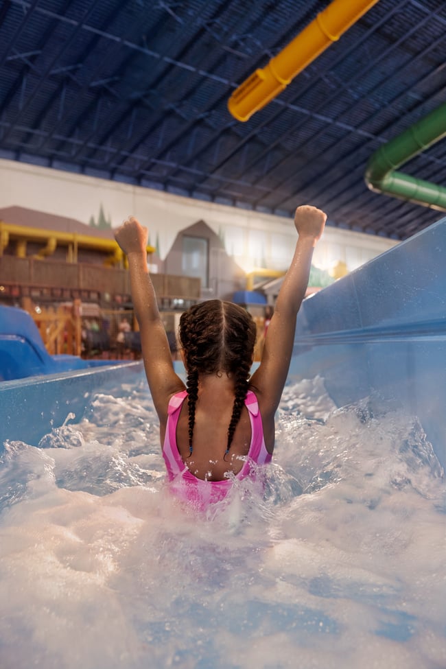 Child celebrating in water slide at indoor water park.