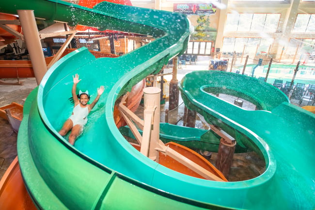 Child sliding down bright turquoise water slide with hands raised.