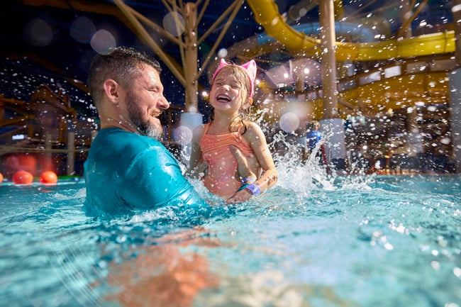 Smiling father and daughter laughing and splashing in a water park pool