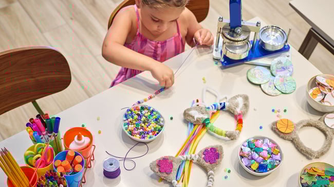 Young girl crafting with beads and supplies at a table.